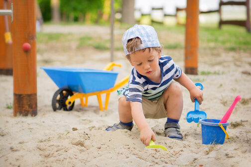 Kleiner Junge spielt im Sandkasten und hält eine gelbe Schaufel in der Hand