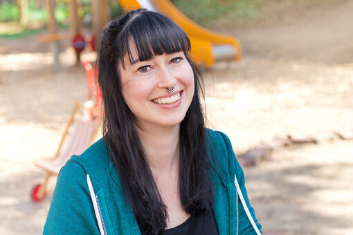 Eine junge Frau mit schwarzen Haaren auf dem Spielplatz, im Hintergrund ist eine Rutsche.