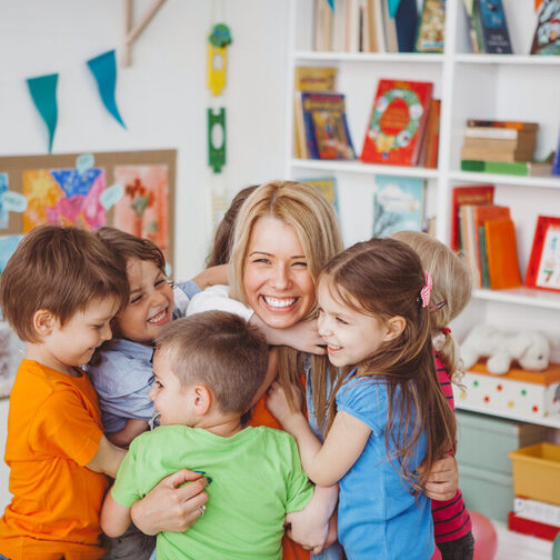 Eine junge Frau wird von einer Kindergruppe umarmt.