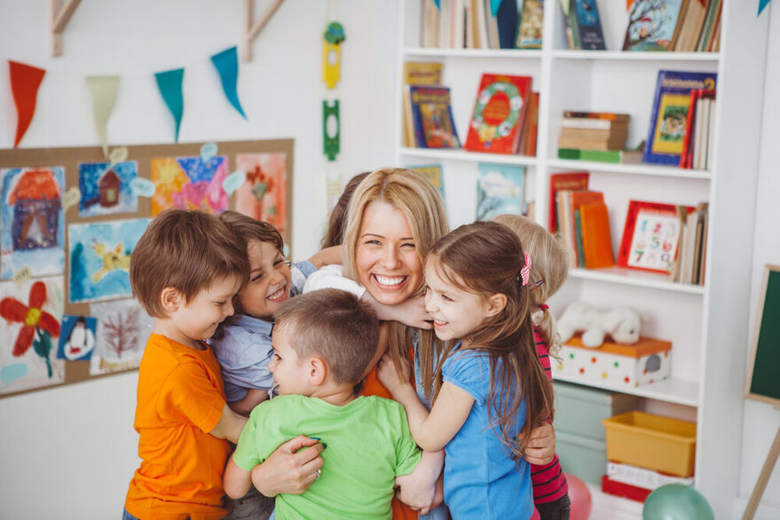 Eine junge Frau wird von einer Kindergruppe umarmt.