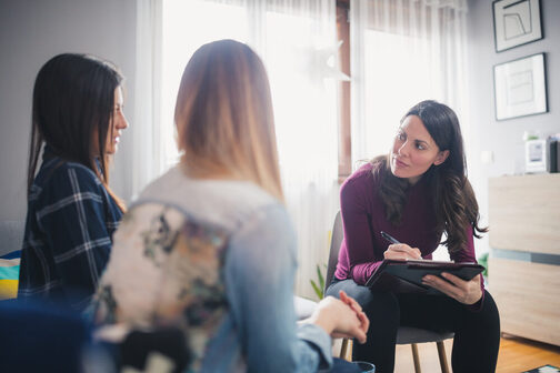 Sozialarbeiterin sitzt mit zwei Frauen im Wohnzimmer und notiert etwas auf einem Blatt